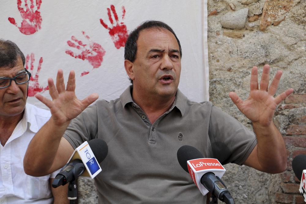 In this photo taken on Sept. 2019, the former mayor of Riace, in Southern Italy, Domenico Mimmo Lucano receives media attention.  A court in southern Italy on Thursday, Sept. 30, 2021, convicted Lucano, who was mayor of a tiny town dubbed “the town of welcome” of aiding illegal immigration and sentenced him to 13 years and two months in prison. Prosecutors alleged that Lucano facilitated marriages of convenience between Italian men in the town of Riace and foreign women to get the women Italian residency permits. (Luigi Salsini/LaPresse via AP)