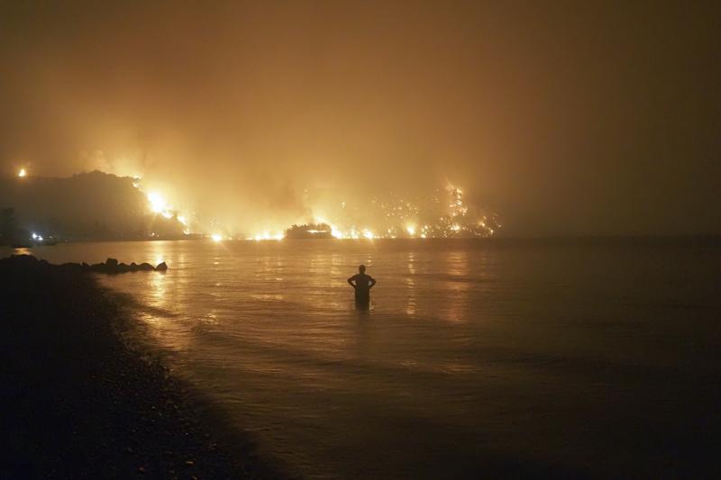 FILE - In this file photo dated Friday, Aug. 6, 2021, a man watches as wildfires approach Kochyli beach near Limni village on the island of Evia, about 160 kilometers (100 miles) north of Athens, Greece.  A new massive United Nations science report is scheduled for release Monday Aug. 9, 2021, reporting on the impact of global warming due to humans. (AP Photo/Thodoris Nikolaou)