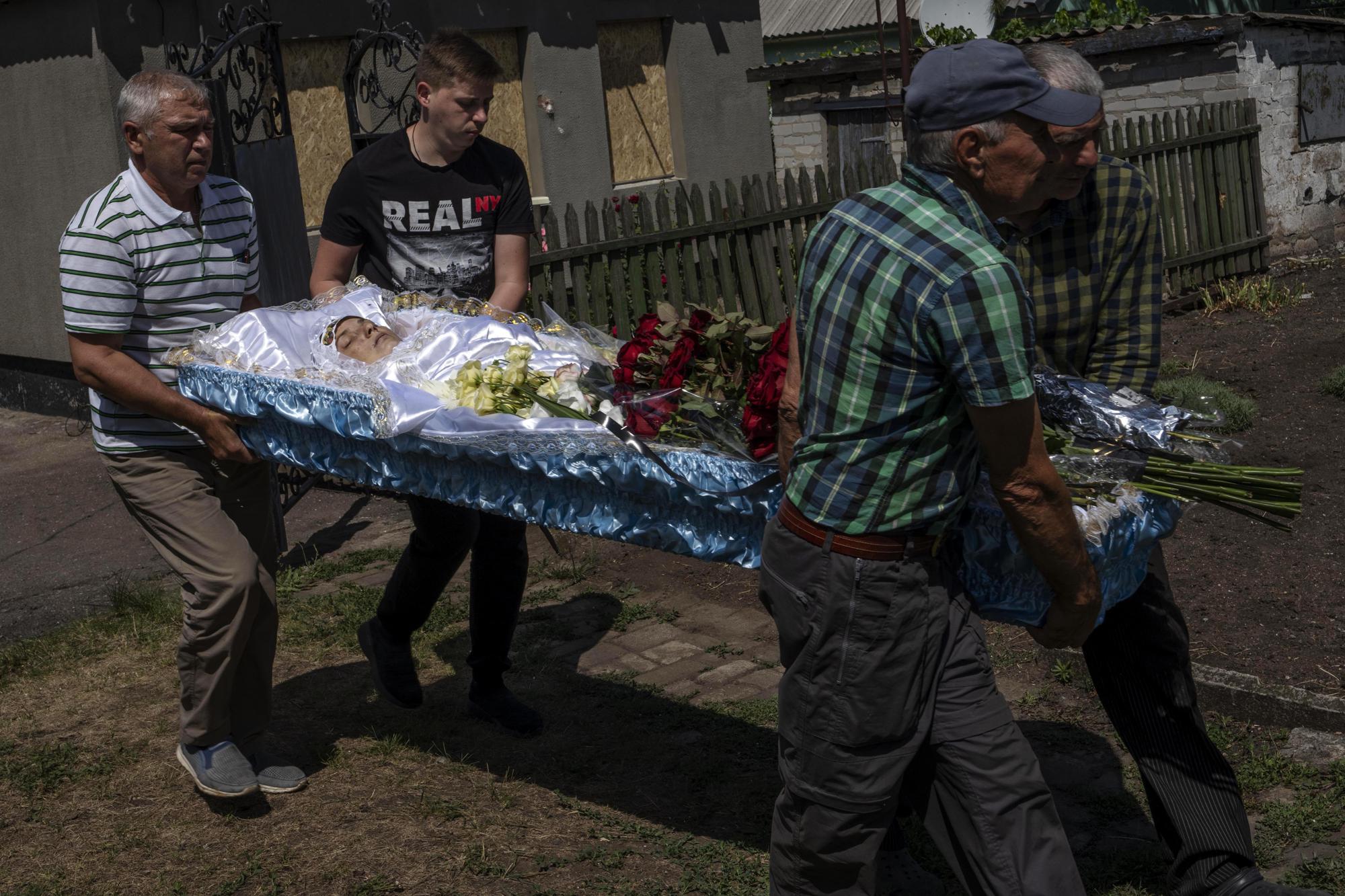 Men carry the lifeless body of 35-year-old Anna Protsenko, who was killed in a Russian rocket attack, during her funeral procession, on the outskirts of Pokrovsk, eastern Ukraine, Monday, July 18, 2022. Protsenko was killed two days after coming home. She had done what authorities wanted, evacuating eastern Ukraine's Donetsk region as Russian forces move closer, but starting a new life elsewhere was uncomfortable and expensive. (AP Photo/Nariman El-Mofty)