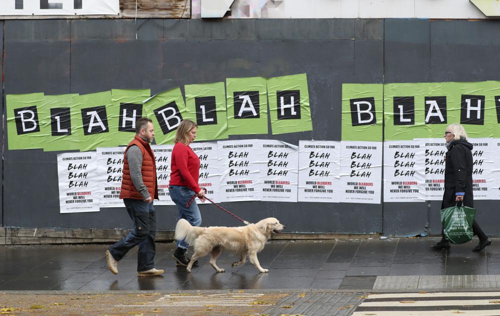 Tres personas pasan delante de carteles colocados por activistas por el clima antes de una protesta el viernes 5 de noviembre de 2021 por las calles de Glasgow, Escocia, la ciudad donde se lleva a cabo la cumbre COP26. (AP Foto/Scott Heppell)