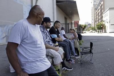 William Nonluecha, foreground, and his friends sit in the shade, Wednesday, July 27, 2022, in Portland, Ore., as a heat wave envelopes the Pacific Northwest. Nonluecha, who lives in a tent, says the heat becomes unbearable inside it when temperatures rise and he stays cool by going to public libraries and riding public transit. "I got a flier yesterday … about the cooling shelter but it was too late," Nonluecha says. (AP Photo/Gillian Flaccus)