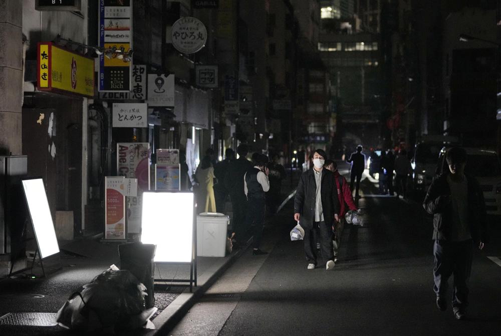 People walk on a street during a black out in Tokyo Thursday, March 17, 2022, following an earthquake. A powerful earthquake struck off the coast of Fukushima in northern Japan on Wednesday evening, triggering a tsunami advisory and plunging more than 2 million homes in the Tokyo area into darkness. (Kyodo News via AP)