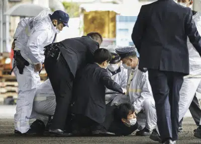 Varios policías sujetan a un hombre tras derribarlo, después de que supuestamente arrojó un objeto explosivo hacia el primer ministro japonés, Fumio Kishida, mientras visitaba el puerto de Saikazaki para un evento de campaña electoral en Wakayama, en el oeste de Japón, el sábado 15 de abril de 2023. Kishida fue evacuado ileso, dijeron las autoridades. (Kyodo News vía AP)