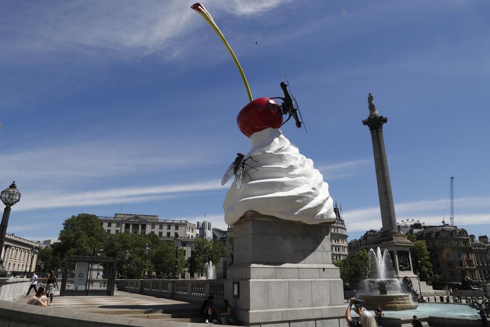 FILE - In this Thursday, July 30, 2020 file photo, a woman takes a photo on her phone of the new work of art entitled 'The End' by artist Heather Phillipson which was unveiled on the fourth plinth in Trafalgar Square in London. A sculpture symbolizing Britain’s complex colonial ties and an artwork featuring the faces of 850 transgender people are set to go on display in Trafalgar Square, one of London’s highest-profile venues for public art. City officials on Monday July 5, 2021, announced the next two works to occupy the “fourth plinth” in the central London square. (AP Photo/Alastair Grant, File)