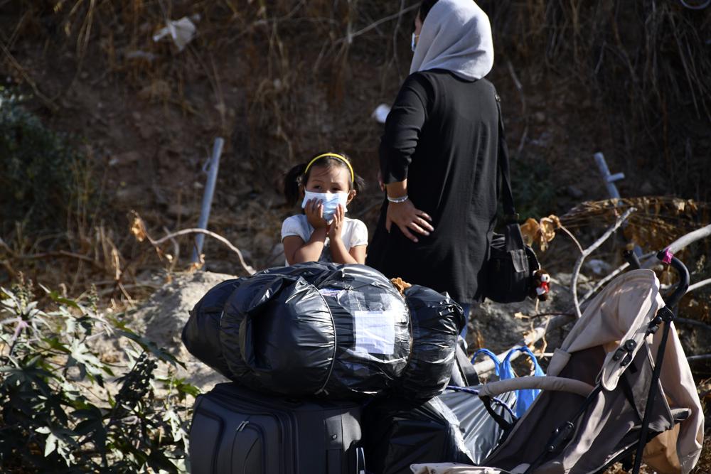 Migrants with their belongs wait to leave from an overcrowded refugee camp at the port of Vathy on the eastern Aegean island of Samos, Greece, Monday, Sept. 20, 2021. The transfer of all the migrants to the new €43 million ($50 million) closed monitored facility began Monday and be completed by Wednesday. (AP Photo/Michael Svarnias)