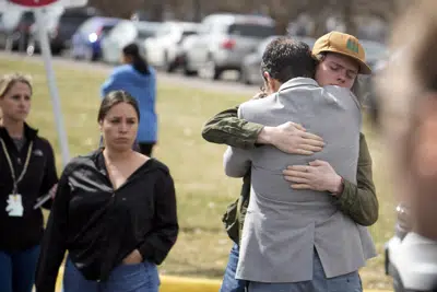 Un alumno, a la derecha, abraza a un padre al reunirse después de un tiroteo escolar en la escuela East High School, el miércoles 22 de marzo de 2023, en Denver. (AP Foto/David Zalubowski)