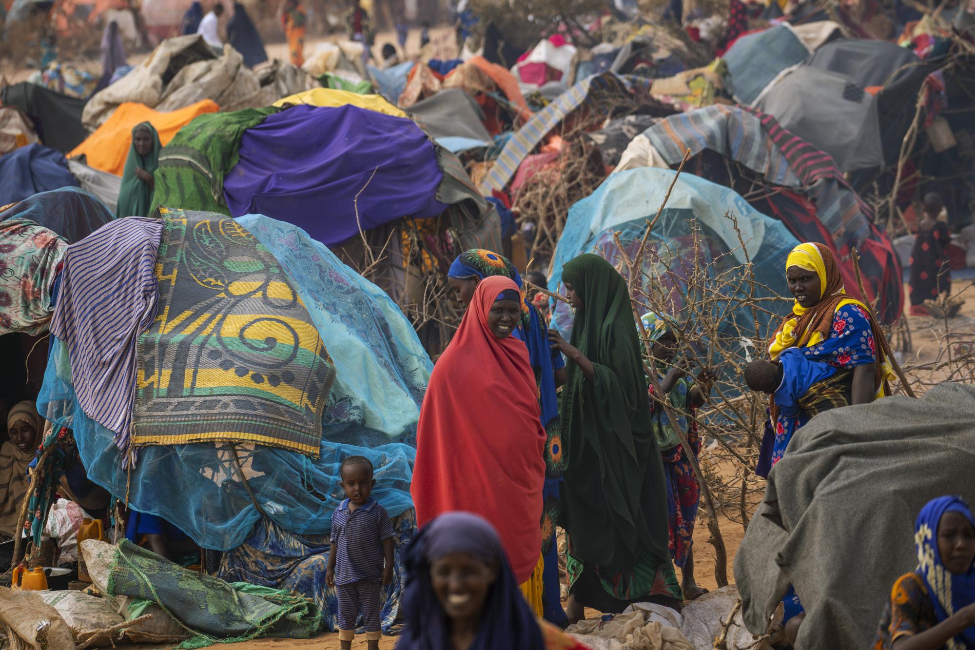 People walk through a displacement camp outskirts of Dollow, Somalia, on Monday, Sept. 19, 2022.  Somalia is in the midst of the worst drought anyone there can remember. A rare famine declaration could be made within weeks. Climate change and fallout from the war in Ukraine are in part to blame. (AP Photo/Jerome Delay)