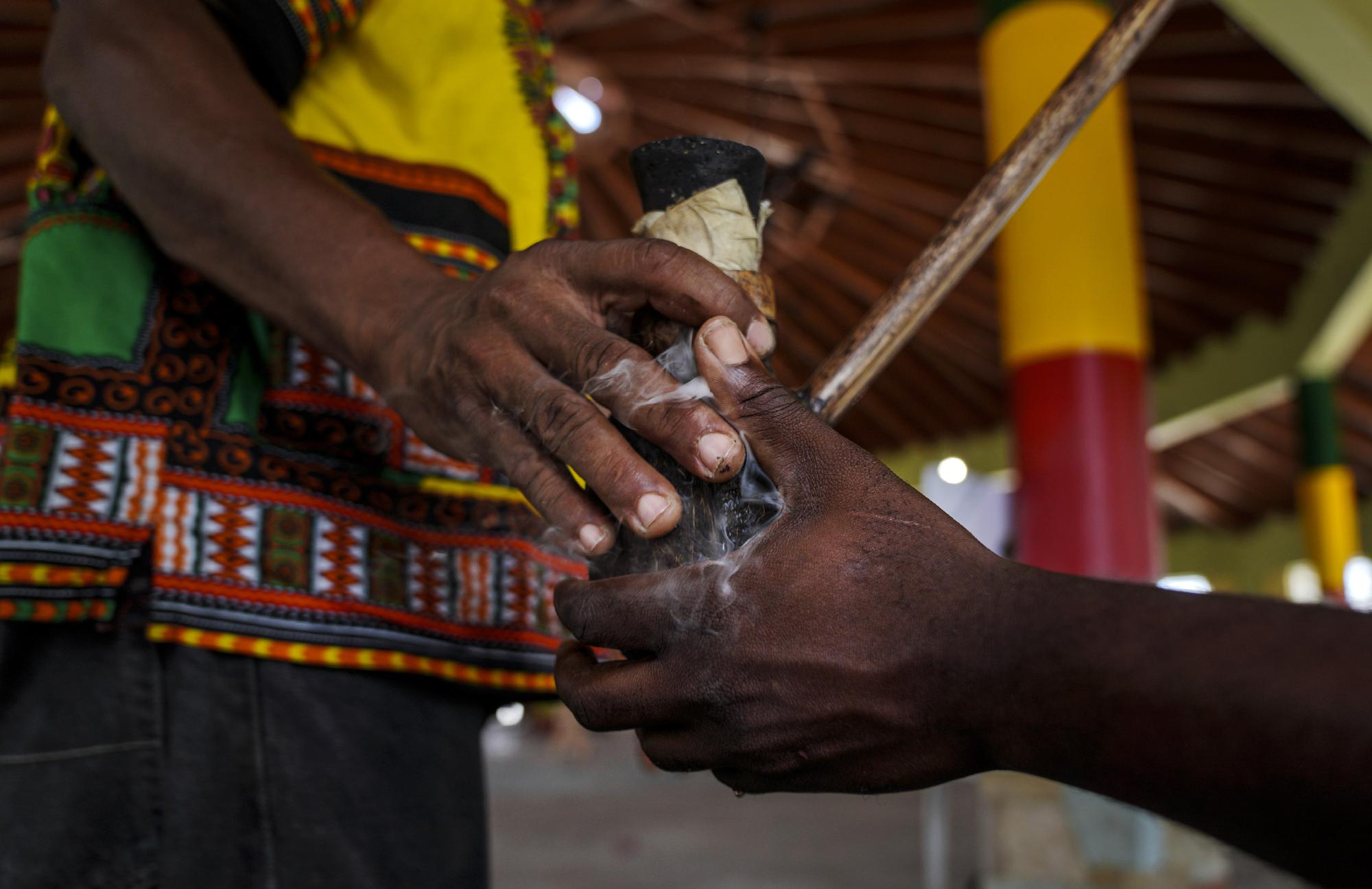 Rastafaris, Ras Wilkins, left, and Ras Richie, pass a chalice pipe made of coconut and clay, in which they smoke marijuana, during service in the tabernacle on Sunday, May 14, 2023, on the Ras Freeman Foundation for the Unification of Rastafari property in Liberta, Antigua. (AP Photo/Jessie Wardarski)