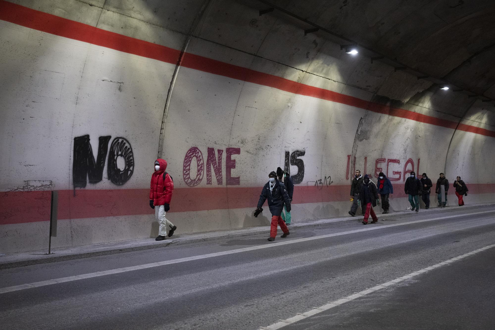 Migrants headed to France from Italy walk past graffiti that reads "No One is Illegal" in a tunnel leading to the French-Italian border, Saturday, Dec. 11, 2021. (AP Photo/Daniel Cole)