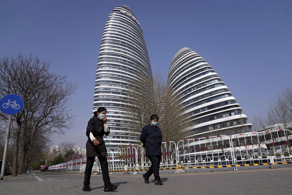 Women wearing face masks to help protect from the coronavirus walk by a barricaded Galaxy Soho commercial office building which was locked down for health monitoring following a COVID-19 case detected in the area, Tuesday, April 5, 2022, in Beijing. China has sent more than 10,000 health workers from across the country to Shanghai, including 2,000 military medical staff, as it struggles to stamp out a rapidly spreading COVID-19 outbreak in China's largest city. (AP Photo/Andy Wong)