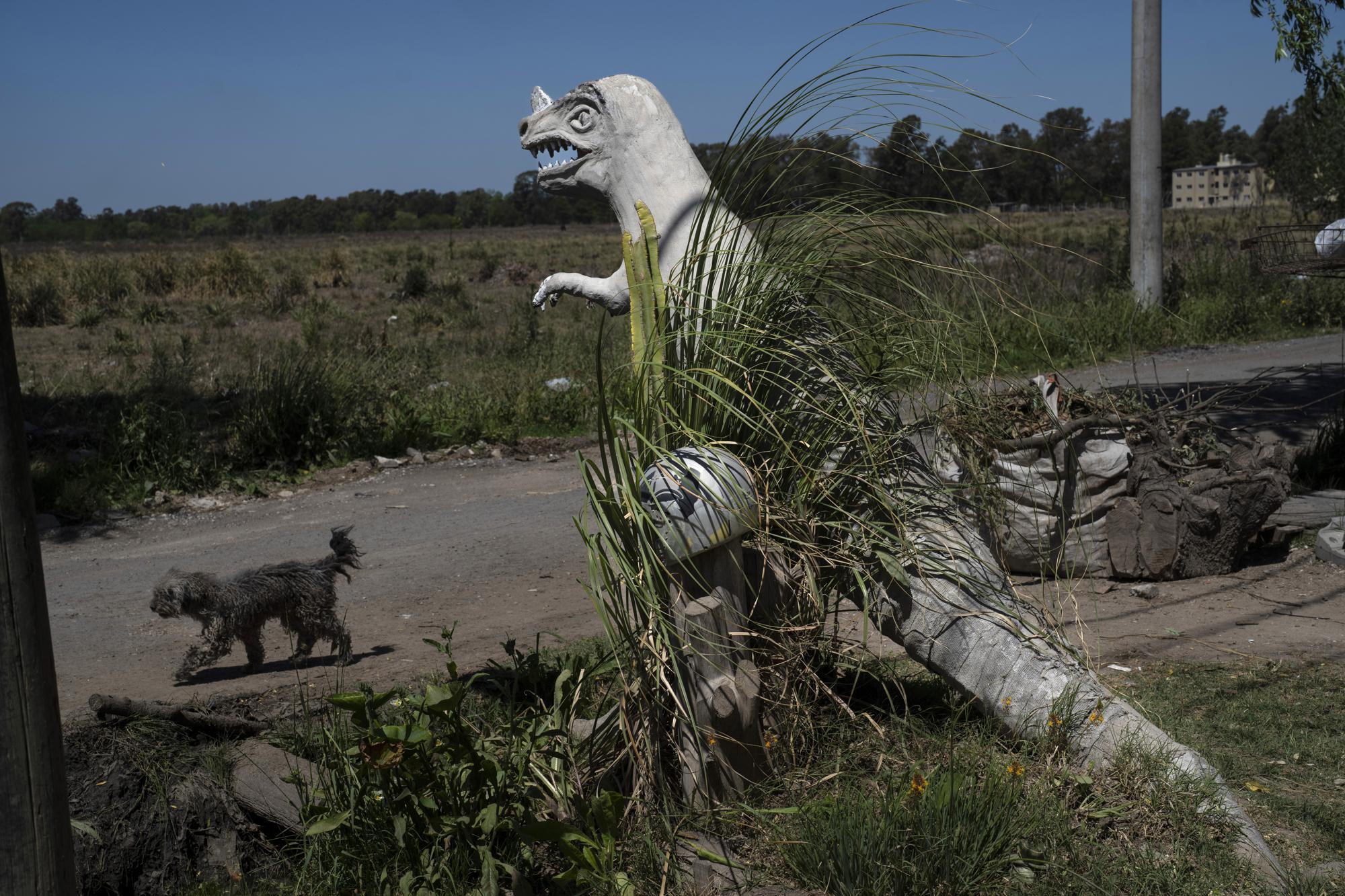 Un perro pasa frente a una escultura de un dinosaurio exhibida en el patio delantero del albañil Daniel Niz en el barrio Sol de Oro de Ezeiza, Argentina, el martes 8 de noviembre de 2022. (AP Foto/Rodrigo Abd)