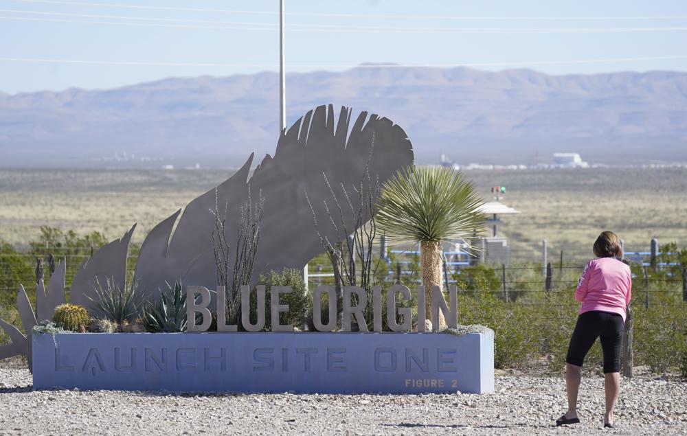 Carol Larro of Atlanta, Ga., checks out the sign at the entrance to the Blue Origin launch site near Van Horn, Texas, Monday, Oct. 11, 2021. Tuesday's launch has been pushed to Wednesday due to weather. (AP Photo/LM Otero)