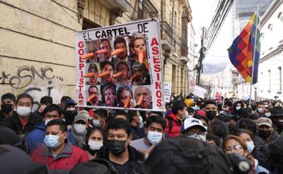 Manifestantes marchan sosteniendo una pancarta con un mensaje en referencia a la expresidenta interina de Bolivia, Jeanine Áñez, sus ministros y líderes de la oposición, mientras partidarios y críticos se reúnen frente a la Corte de Justicia en el primer día de juicio a Áñez en La Paz, Bolivia, el jueves 10 de febrero de 2022. (AP Foto/Juan Karita)