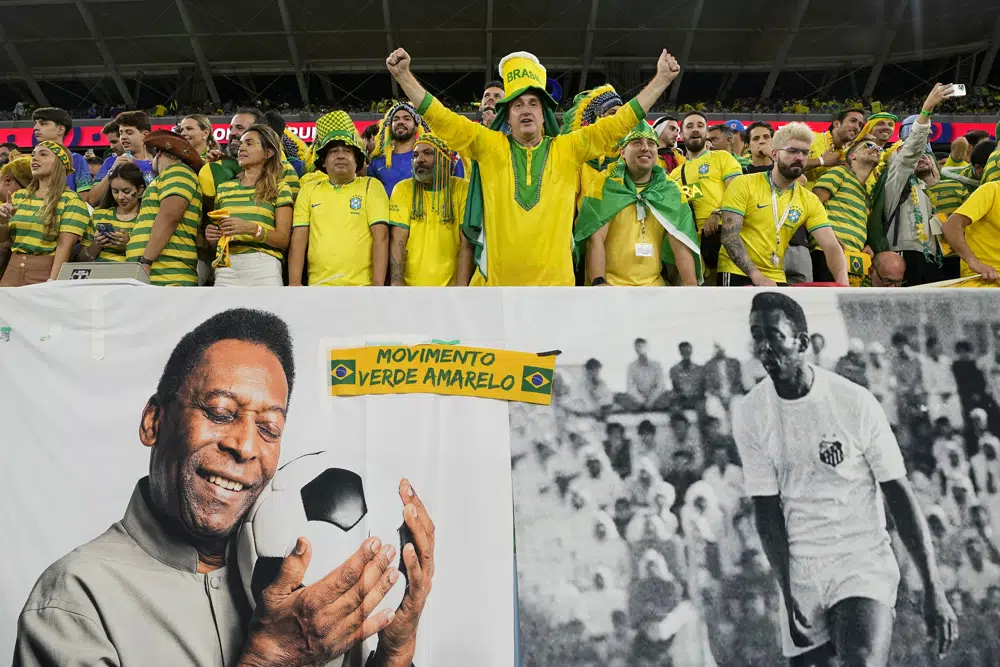 Aficionados de Brasil alientan a la selección detrás de un cartel con imágenes de Pelé, el lunes 5 de diciembre de 2022, antes de un partido del Mundial ante Corea del Sur en Al Rayán, Qatar (AP Foto/Martin Meissner)