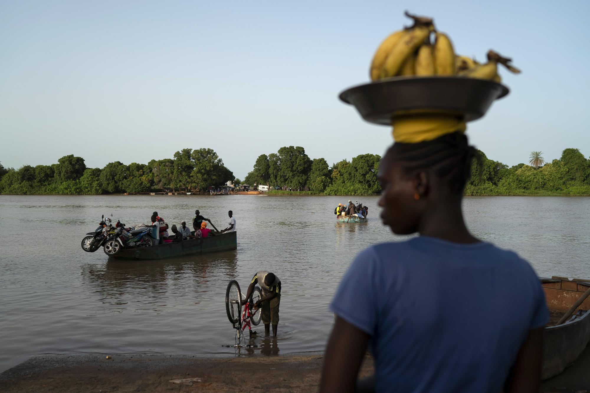 Carrying bananas for sale, a woman waits for the boat to cross the Gambia river in Bansang, Gambia, Tuesday, Sept. 28, 2021. As health officials in Gambia and across Africa urge women to be vaccinated, they've confronted hesitancy among those of childbearing age. Although data on gender breakdown of vaccine distribution are lacking globally, experts see a growing number of women in Africa's poorest countries consistently missing out on vaccines. (AP Photo/Leo Correa)