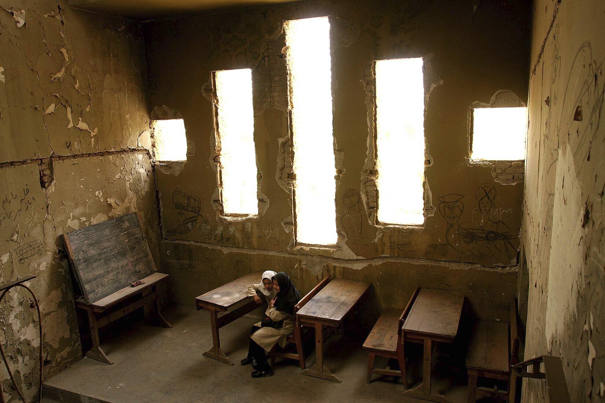 Basera, 13, right, and Saira, 10, wait for their class to begin at Loy Ghar school, in the bombed-out carcass of the Kabul Theater in Afghanistan's capital, April 20, 2005. The bullet-riddled building has become a place of hope for more than 400 students looking to rebuild their lives after decades of war. Classrooms have sprung up near windows or where bombs have destroyed enough of the wall to allow in sunlight. (AP Photo/Tomas Munita)