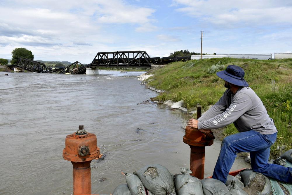 Kelly Hitchcock closes an irrigation ditch just downriver from a bridge collapse at the Yellowstone River near Columbus, Mont., on Saturday, June 24, 2023. The bridge collapsed overnight, causing a train that was traveling over it to plunge into the water below. (AP Photo/Matthew Brown)