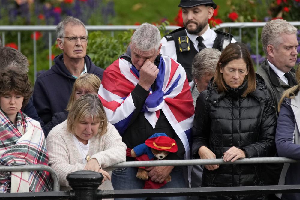 A person holding a Paddington Bear stuffed toy stands with members of the public outside Buckingham Palace waiting to watch Queen Elizabeth II funeral procession, in central London Monday, Sept. 19, 2022. The Queen, who died aged 96 on Sept. 8, will be buried at Windsor alongside her late husband, Prince Philip, who died last year. (AP Photo/Christophe Ena, Pool)