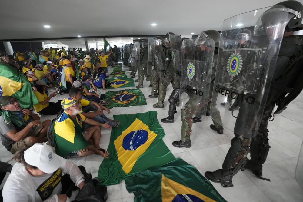 FILE - Supporters of Brazil's former President Jair Bolsonaro, sit in front of police inside the Planalto Palace after storming it, in Brasilia, Brazil, Jan. 8, 2023. While hundreds of civilians who participated on Jan. 8 have been jailed and dozens indicted, service members have thus far been spared. (AP Photo/Eraldo Peres, File)