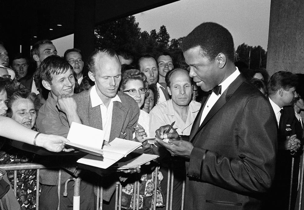 FILE - Sidney Poitier signs autographs before the opening of the 14th International Film Festival at the West Berlin congress hall on June 26, 1964 in Berlin. Poitier, the groundbreaking actor and enduring inspiration who transformed how Black people were portrayed on screen, became the first Black actor to win an Academy Award for best lead performance and the first to be a top box-office draw, died Thursday, Jan. 6, 2022 in the Bahamas. He was 94. (AP Photo/Edwin Reichert, File)