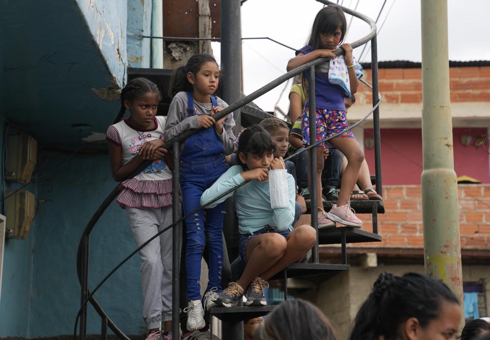 Girls watch an event for children at a soup kitchen in the Antimano neighborhood of Caracas, Venezuela, Tuesday, July 27,2021. The soup kitchen was celebrating a belated national children's day with different cultural activities, amid the new coronavirus pandemic. (AP Photo/Ariana Cubillos)