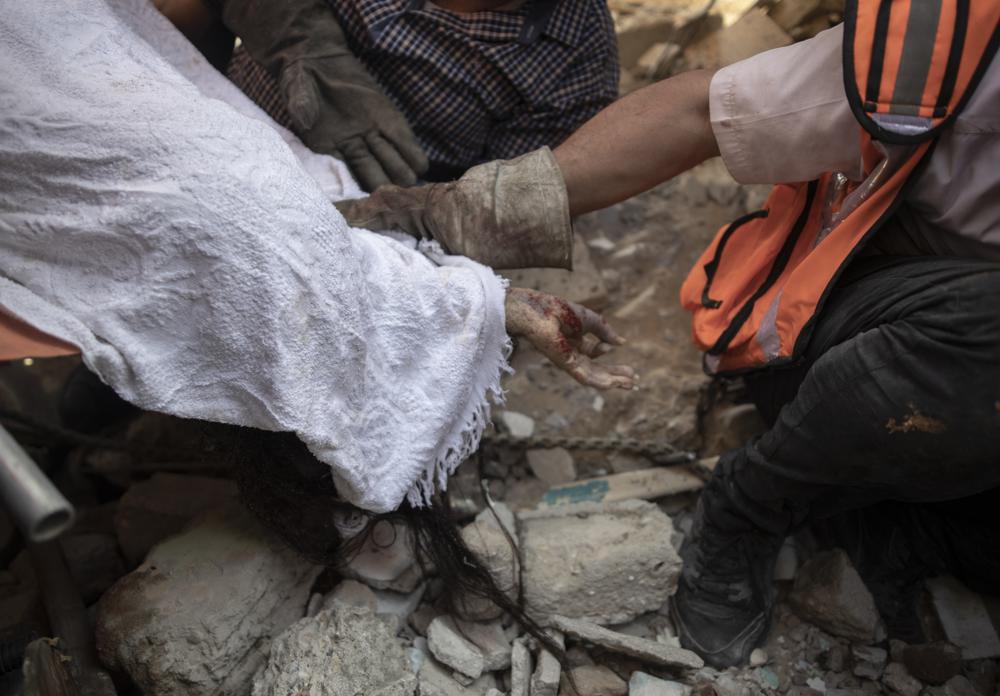 File - In this Sunday, May 16, 2021 file photo, Palestinian rescuers remove the covered body of a woman of al-Kawlak family from under the rubble of one of the destroyed residential buildings following deadly Israeli airstrikes in Gaza City. The single deadliest bombing raid of Israel's fourth war with Hamas collapsed two apartment buildings and killed 22 members of the extended al-Kawlak family, including a 6-month-old boy and his 89-year-old great-grandfather (AP Photo/Khalil Hamra,File)