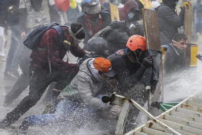 Manifestantes antigubernamentales se protegen de un cañón de agua de la policía durante los enfrentamientos en Madrid, en las afueras de Bogotá, Colombia, el viernes 28 de mayo de 2021. Según un informe de Amnistía Internacional y otras organizaciones, 103 colombianos sufrieron traumas oculares por el presunto uso desproporcionado de la fuerza por parte de agentes de la policía durante las protestas de este año. (AP Foto/Iván Valencia)