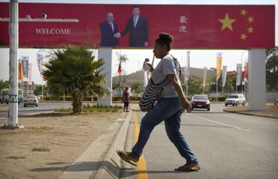 ARCHIVO - Una mujer cruza la calle cerca de una valla publicitaria que conmemora la visita de Estado del presidente chino Xi Jinping en Port Moresby, Papúa Nueva Guinea, el 15 de noviembre de 2018. China quiere que 10 pequeñas naciones del Pacífico respalden un acuerdo radical que abarque todo, desde la seguridad hasta la pesca, en lo que un líder advierte que es un intento "revolucionario" de Beijing para arrebatar el control de la región. (AP Photo/Mark Schiefelbein, Archivo)