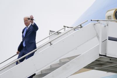 El presidente de Estados Unidos, Joe Biden, con la mascarilla en una mano, saluda mientras baja del Air Force One en el aeropuerto internacional Capital Region, el 5 de octubre de 2021, en Lansing, Michigan. (AP Foto/Evan Vucci)