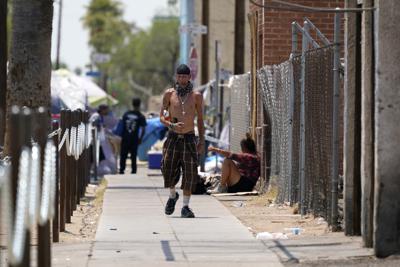 Un hombre camina junto a un campamento de personas sin hogar bajo temperaturas por arriba de los 46 grados Celsius (115 Fahrenheit), el jueves 17 de junio de 2021, en Phoenix. (AP Foto/Ross D. Franklin)
