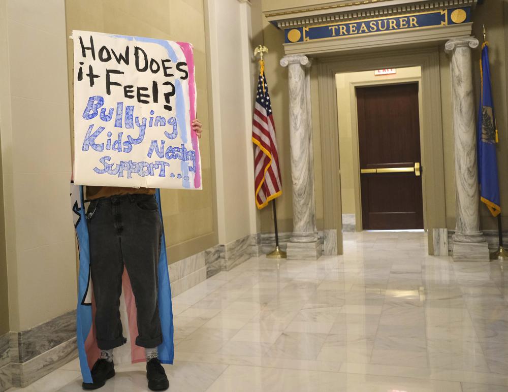 Kara Klever holds a sign in protest in the hall outside of the Blue Room as Governor Kevin Stitt signs a bill into law that prevents transgender girls and women from competing on female sports teams at the Capitol Wednesday, March 30, 2022 in Oklahoma City, Oka. The bill, which easily passed the Republican-led House and Senate mostly along party lines, took effect immediately with the governor's signature. It applies to female sports teams in both high school and college.  (Doug Hoke /The Oklahoman via AP)
