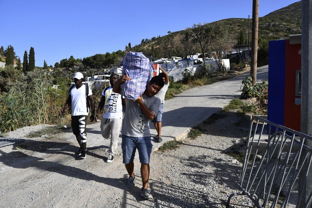 Migrants carry their belongs as they leave from an overcrowded refugee camp at the port of Vathy on the eastern Aegean island of Samos, Greece, Monday, Sept. 20, 2021. The transfer of all the migrants to the new €43 million ($50 million) closed monitored facility began Monday and be completed by Wednesday. (AP Photo/Michael Svarnias)