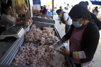 Cindy Cueto revisa contenedores de cabezas y patas de pollo crudas mientras compra para un comedor de beneficencia local en el mercado Juan Velasco en el barrio de Villa El Salvador de Lima, Perú, el martes 12 de abril de 2022. (AP Foto/Martin Mejia)