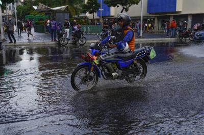 Un hombre en moto cruza un charco en Caracas, Venezuela, 29 de junio de 2022. (AP Foto/Ariana Cubillos)