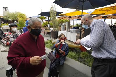 ARCHIVO - En esta foto del 20 de agosto del 2021, el anfitrión Jason Pryor, derecha, revisa las tarjetas de vacunación de identificación de comensales a la entrada del restaurante Waterbar, en San Francisco, California. (AP Foto/Eric Risberg)