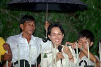 FILE - An aid holds an umbrella over Burmese democratic leader Aung San Suu Kyi during her daily appearance at the gate of her Yangon (formerly known as Rangoon) home from where she greets a crowd of supporters that gathered in the street on July 16, 1995. A court in Myanmar sentenced the country’s ousted leader, Aung San Suu Kyi, to four years in prison on Monday, Dec. 6, 2021, after finding her guilty of incitement and violating coronavirus restrictions, a legal official said. (AP Photo/Anat Givon, File)