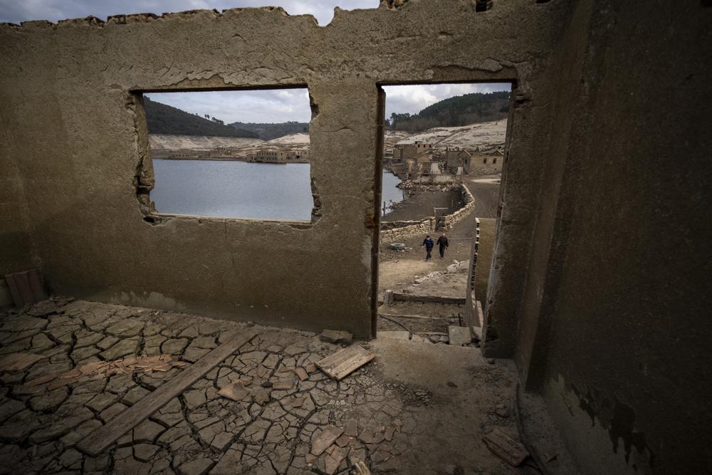 Jose Penín, de 72 años, camina con su hermano Julio, de 78, mientras visitan el antiguo pueblo de Aceredo, sumergido hace tres décadas cuando una presa hidroeléctrica inundó el valle y ahora accesible debido a la sequía en el embalse de Lindoso, en el noroeste de España, el viernes 11 de febrero de 2022. Los tejados asomando en el agua se han convertido en una escena habitual en verano en el embalse de Lindoso, en el noroeste de España. En años especialmente secos aparecían partes del antiguo pueblo, sumergido hace tres décadas cuando una presa hidroeléctrica inundó el valle. Pero nunca había reaparecido el pueblo entero en pleno invierno. (AP Foto/Emilio Morenatti)