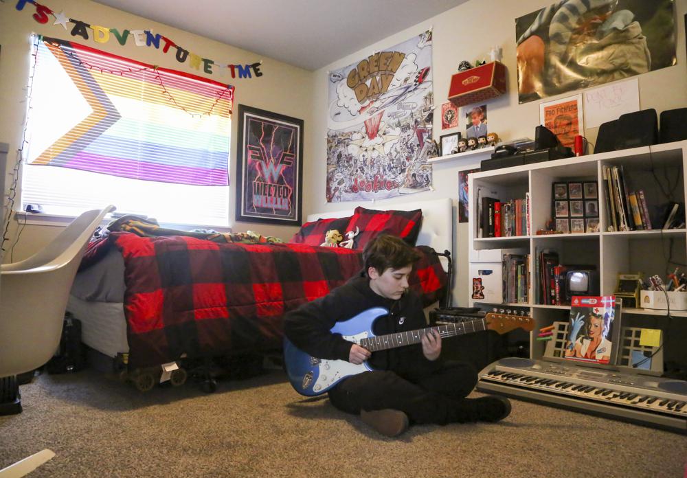 Asher Wilcox-Broekemeier, 13, practices guitar in his bedroom, Monday, March 27, 2023, in Sioux Falls, S.D. When Asher began menstruating, he felt a terrifying disconnect between how his body was changing on the outside and how he felt inside. His mom began researching online to understand what was going on with her son, while Asher’s father, Brian, looked to doctors for expertise. With referrals from his longtime pediatrician, Asher met with therapists and doctors who helped explore his history, personality and feelings over his whole life. (AP Photo/Erin Woodiel)