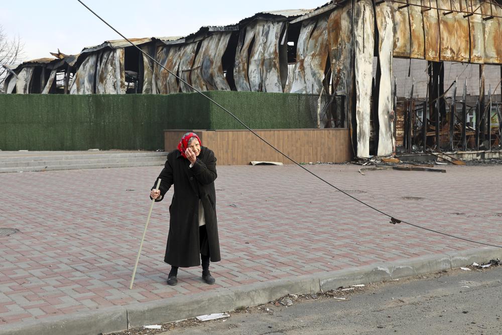 An elderly local resident stands behind a destroyed part of the Illich Iron & Steel Works Metallurgical Plant, the second largest metallurgical enterprise in Ukraine, in an area controlled by Russian-backed separatist forces in Mariupol, Ukraine, Saturday, April 16, 2022. Mariupol, a strategic port on the Sea of Azov, has been besieged by Russian troops and forces from self-proclaimed separatist areas in eastern Ukraine for more than six weeks. (AP Photo/Alexei Alexandrov)