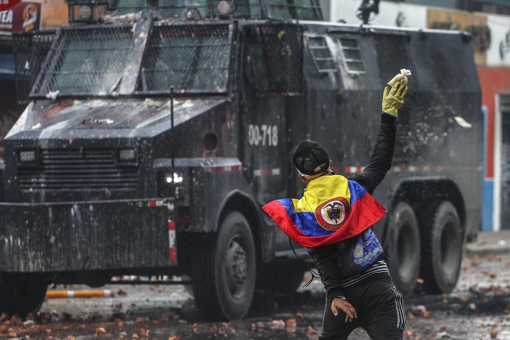 Un manifestante antigubernamental arroja una bolsa de pintura a un vehículo policial durante los enfrentamientos en Madrid, en las afueras de Bogotá, Colombia, el viernes 28 de mayo de 2021. Los colombianos han salido a las calles durante semanas en todo el país después de que el gobierno propuso un impuesto incrementos en servicios públicos, combustibles, salarios y pensiones. (AP Foto/Ivan Valencia)