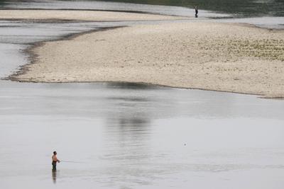 La gente pesca cerca de una planta hidroeléctrica del río Po en San Nazzaro (Italia) el 15 de junio del 2022. El Po se está quedando sin agua y amenaza con causar estregos en el norte de Italia. (AP Photo/Luca Bruno)