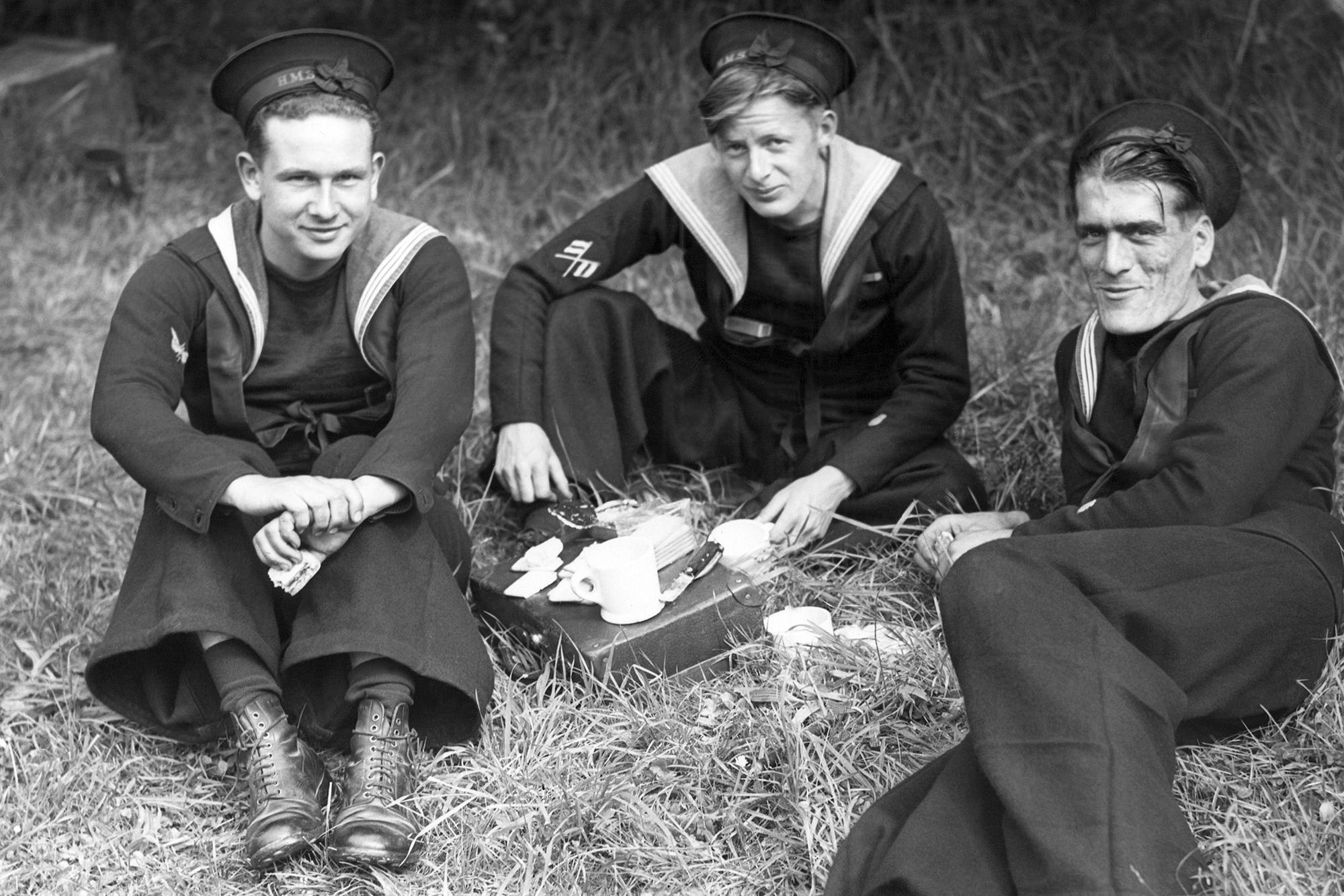 FILE - Men from British Minesweepers operating off the Normandy beachhead enjoy their first shore leave, June 15, 1944. Left to right are: Telegraphis E.F. Guyatt, of Putney, Signalman E.Y. Hammonds of Woodford Essex, and Wireman V.J. Howe of Romford Essex, on the grass with their picnic age. (AP Photo, File)