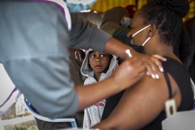 Una mujer keniata recibe una dosis de la vacuna de AstraZeneca donada por Gran Bretaña ante la mirada de su hijo, en el estado de Makongeni, Nairobi, Kenia, el sábado 14 de agosto de 2021. (AP Foto/Brian Inganga)