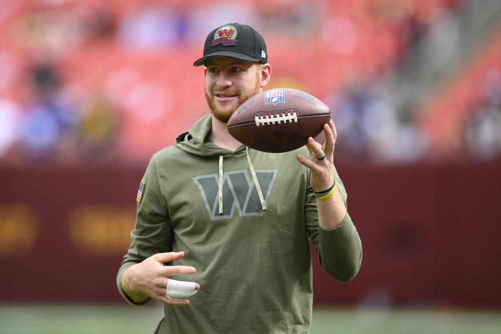 Injured Commanders quarterback Carson Wentz flips a football as he watches practice before the start of an NFL football game against the Minnesota Vikings, Sunday, Nov. 6, 2022, in Landover, Md. (AP Photo/Nick Wass)