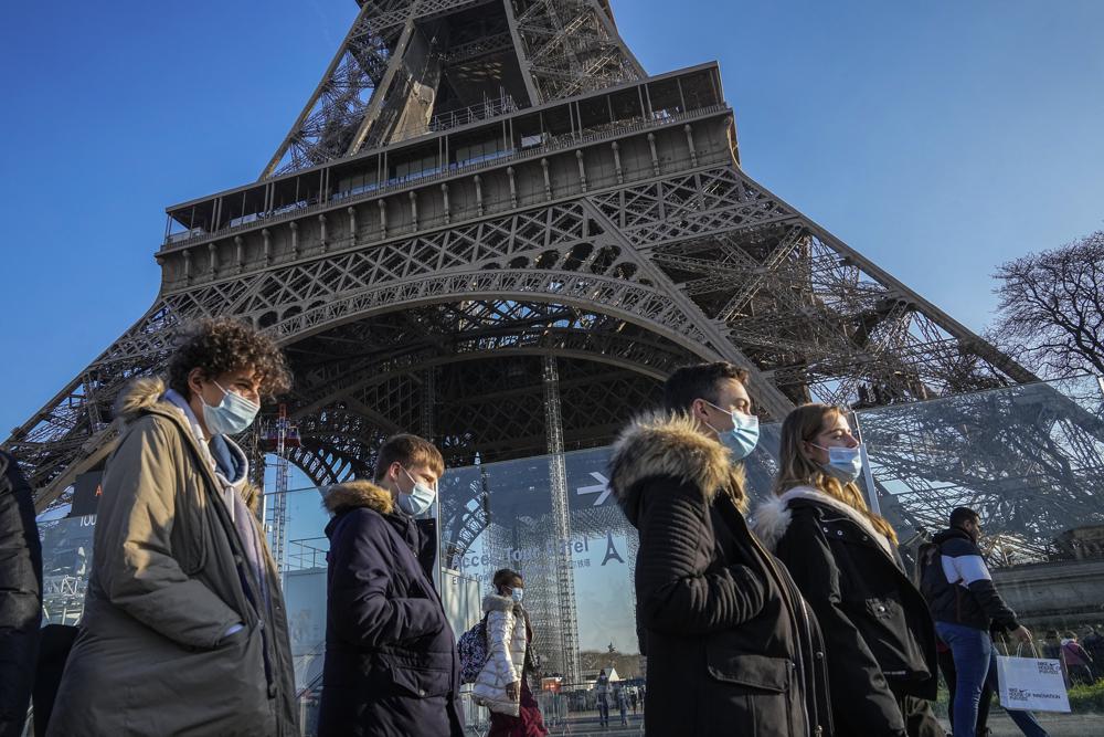 People wearing face masks to protect against COVID-19 walk past the Eiffel Tower in Paris, Tuesday, Dec. 21, 2021. Nations across Europe have moved to reimpose tougher measures to stem a new wave of COVID-19 infections spurred by the highly transmissible omicron variant. (AP Photo/Michel Euler)