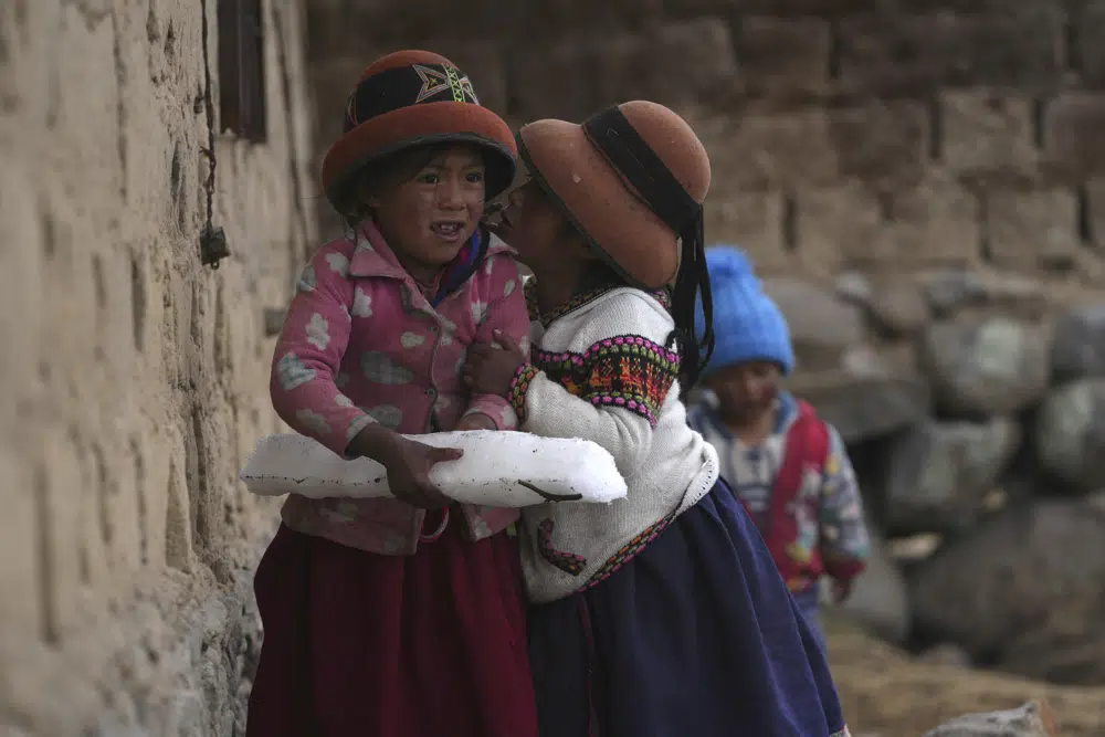 Niñas juegan con un bloque de hielo formado por aguanieve que cayó el día anterior sobre la comunidad de Cconchaccota, en la región Apurímac de Perú, el sábado 26 de noviembre de 2022. (AP Foto/Guadalupe Pardo)