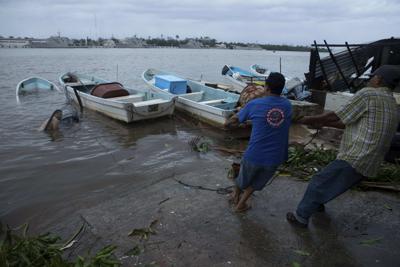 Los pescadores intentan tirar de un bote que fue inundado por el huracán Rick en Lázaro Cárdenas, México, el lunes 25 de octubre de 2021. (AP Foto/Armando Solis)
