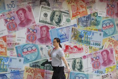 Una mujer pasa frente a una casa de cambio decorada con divisas de todo el mundo en Hong Kong el 6 de agosto del 2019. Un dólar fuerte respecto al resto de las divisas hace que aumenten las posibilidades de una recesión mundial. (AP Photo/Kin Cheung, File)