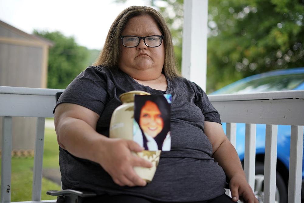 Kelly Titchenell sits on her porch in Mather, Pa., holding a photo of her mother Diania Kronk, and an urn containing her mother's ashes, Thursday, July 7, 2022. A Greene County, Pa., detective last week filed charges against 911 operator Leon “Lee” Price, 50, of Waynesburg, in the July 2020 death of Diania Kronk, 54, based on Price's reluctance to dispatch help without getting more assurance that Kronk would actually go to the hospital. (AP Photo/Gene J. Puskar)