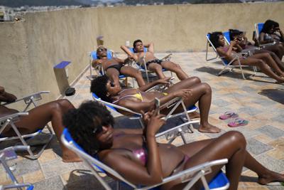 Varias personas descansan en busca de obtener unas líneas definidas de bronceado en bikinis creados con cinta aislante en el salón de bronceado Sabrina Bronze establecido en una azotea en la favela Turano, en Río de Janeiro, Brasil, el jueves 27 de enero de 2022. (AP Foto/Silvia Izquierdo)